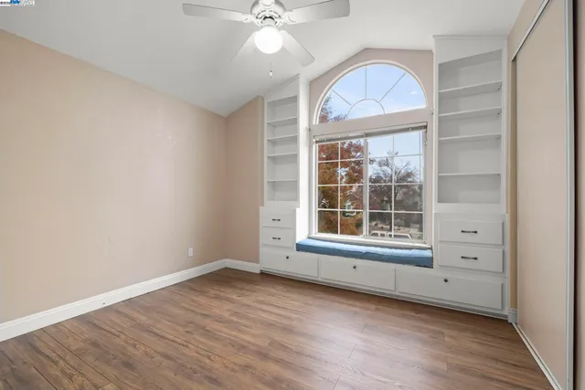 an empty room with wooden floor fan and windows