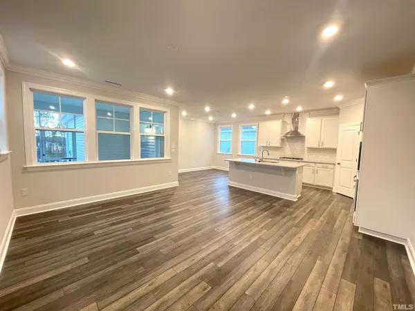 a view of an empty room with wooden floor and a kitchen