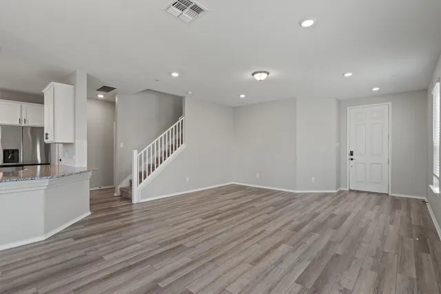a view of an empty room with wooden floor and a kitchen