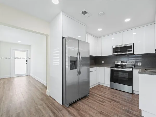 a kitchen with stainless steel appliances granite countertop a refrigerator a sink dishwasher a stove and white countertops with wooden floor