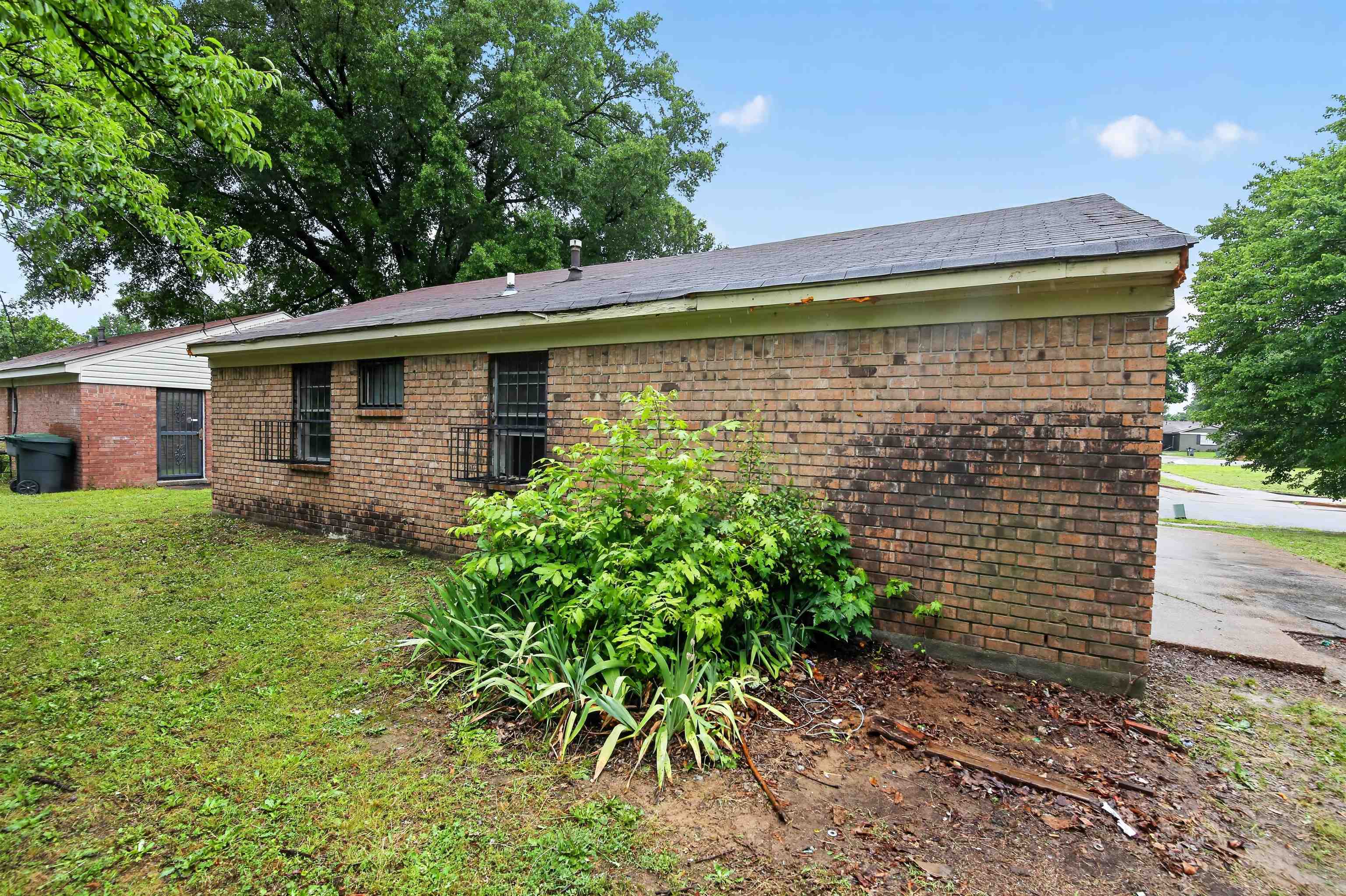 3451 Birdsong Ferry Road Memphis, TN 38118 - Photo 5 of 27 Brick exterior with a dark shingle roof, featuring gridded window security bars and mature landscaping