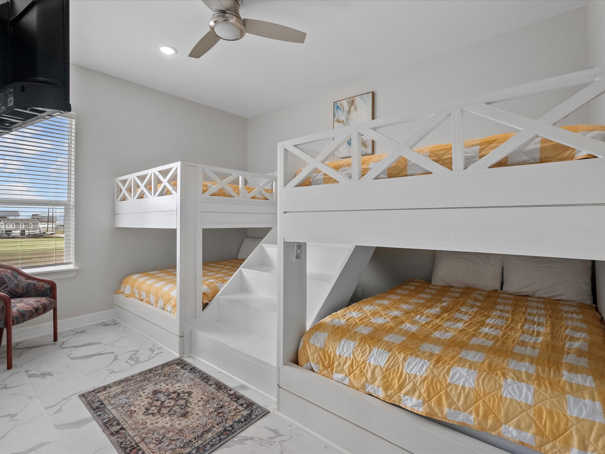 1018 Seashell Drive Surfside Beach, TX 77541 - Photo 25 of 49 This bedroom features white double bunk beds with yellow checkered bedding, a ceiling fan, and a large window providing plenty of natural light. The room has a modern look with marble-like flooring and a small area rug.