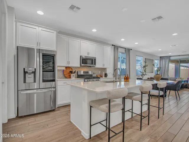 a kitchen with stainless steel appliances a microwave a stove a sink dishwasher a refrigerator with white cabinets and wooden floor