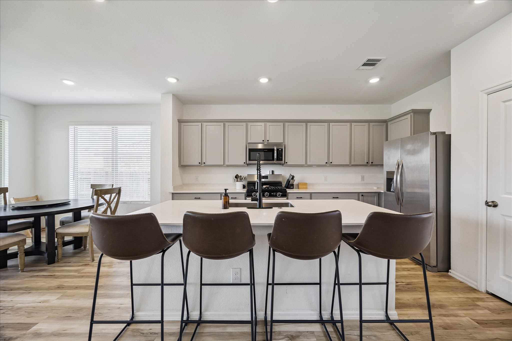 3812 Moss Hl Road Rosenberg, TX 77469 - Photo 12 of 20 A modern kitchen with an open layout, featuring a spacious island with seating for four. The kitchen includes stainless steel appliances, ample cabinetry, and a dining area with natural light from large windows. The overall design is contemporary and inviting.