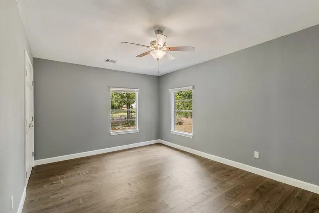 an empty room with wooden floor chandelier fan and windows