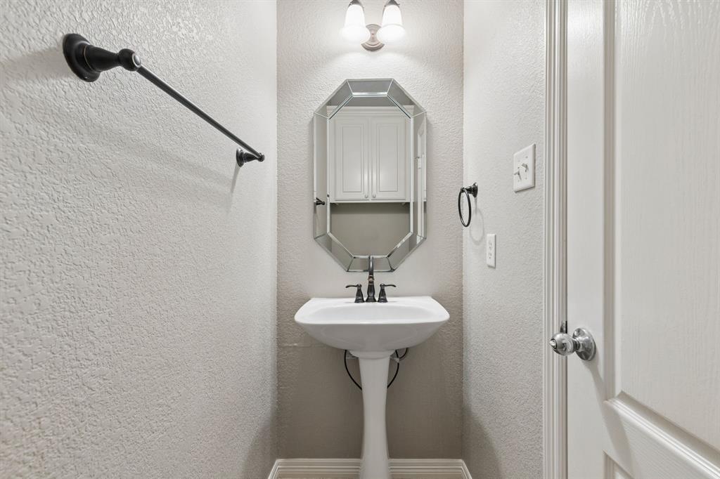317 Singing Quail Trail Haslet, TX 76052 - Photo 19 of 32 Pedestal sink with dark bronze fixtures, octagonal framed mirror, and wall-mounted light fixture