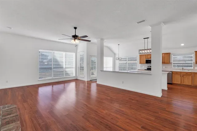 a view of an empty room with wooden floor and a kitchen