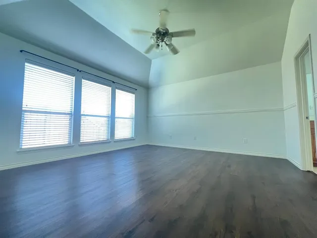 an empty room with wooden floor chandelier fan and windows