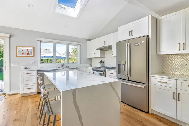 a kitchen with stainless steel appliances granite countertop a refrigerator a stove a sink dishwasher and white cabinets with wooden floor