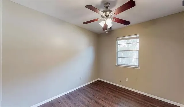 an empty room with wooden floor ceiling fan and windows