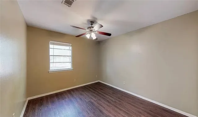 an empty room with wooden floor ceiling fan and window