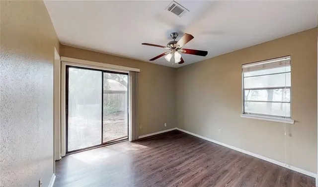 an empty room with wooden floor chandelier fan and windows