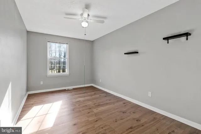 an empty room with wooden floor chandelier fan and windows