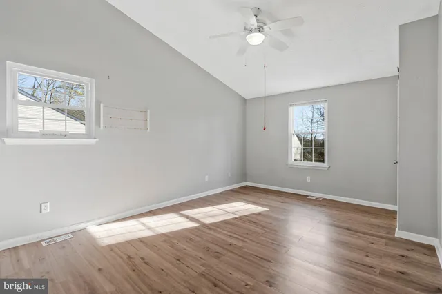 an empty room with wooden floor chandelier fan and windows