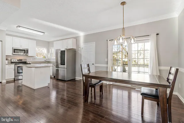 a kitchen with stainless steel appliances granite countertop a stove top oven a refrigerator a dining table and chairs with wooden floor