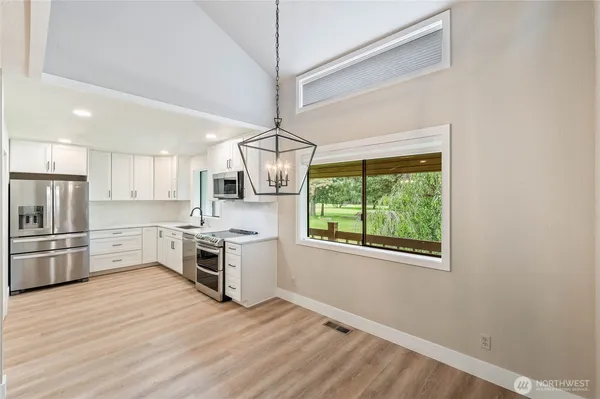 a kitchen with stainless steel appliances a stove top oven a sink dishwasher a refrigerator and a dining table with wooden floor