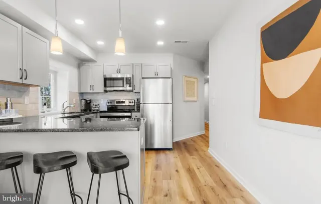 a kitchen with granite countertop a refrigerator a stove a sink and white cabinets with wooden floor