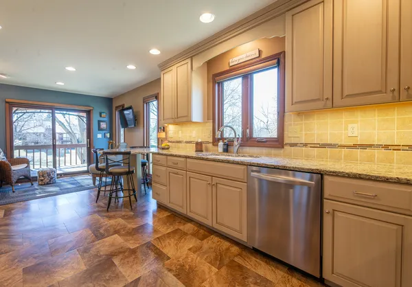 a kitchen with stainless steel appliances granite countertop a refrigerator a sink dishwasher a stove and a dining table with wooden floor