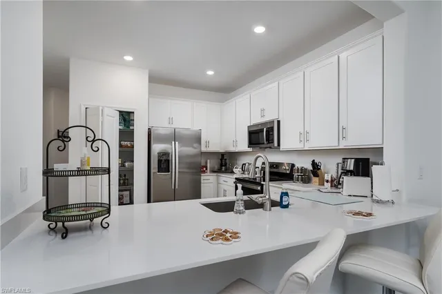 a kitchen with stainless steel appliances a sink a stove a refrigerator cabinets and chairs