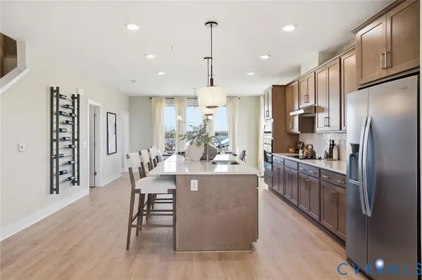 a kitchen with stainless steel appliances kitchen island granite countertop a refrigerator a stove a sink dishwasher and a dining table with wooden floor