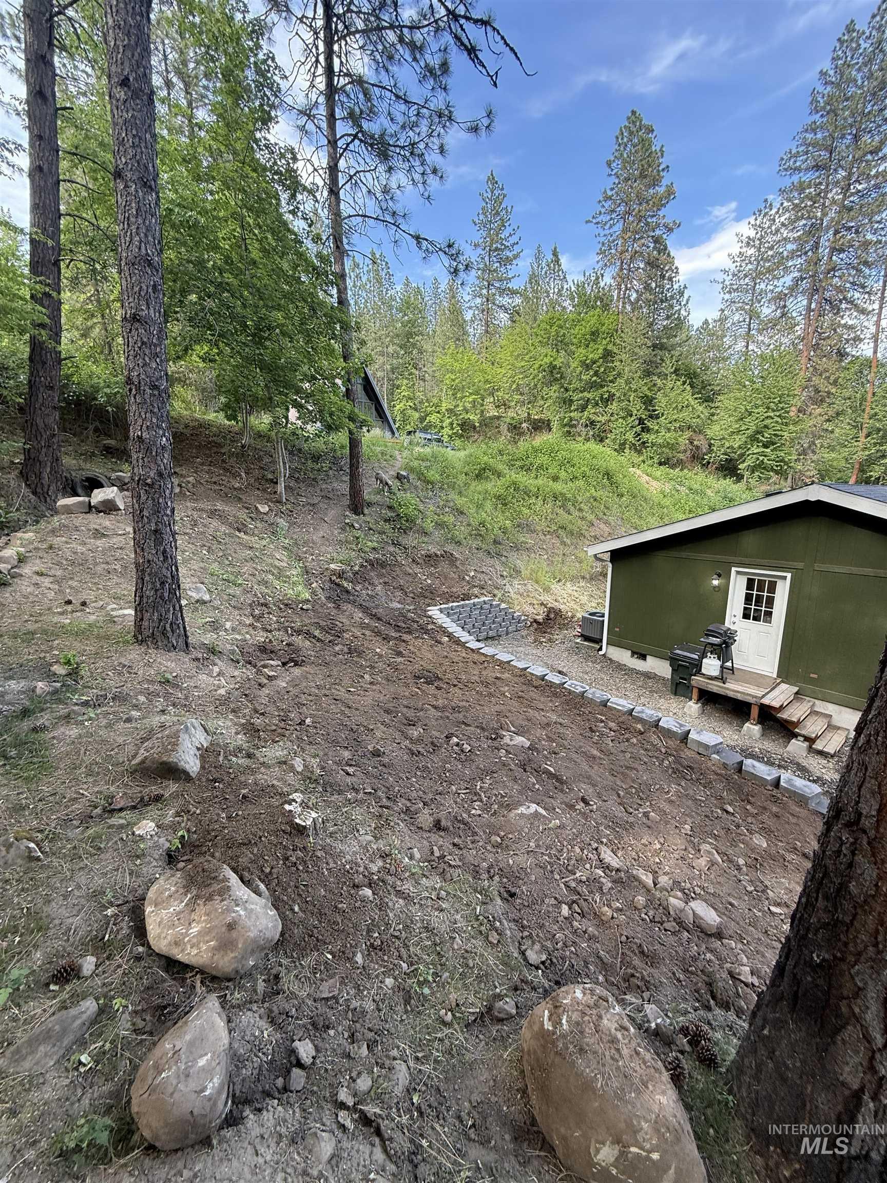 174 Konkolville Road Orofino, ID 83544 - Photo 34 of 43 Wooded hillside property featuring a dark green exterior, a white entry door, wood steps, and a paver stone retaining wall