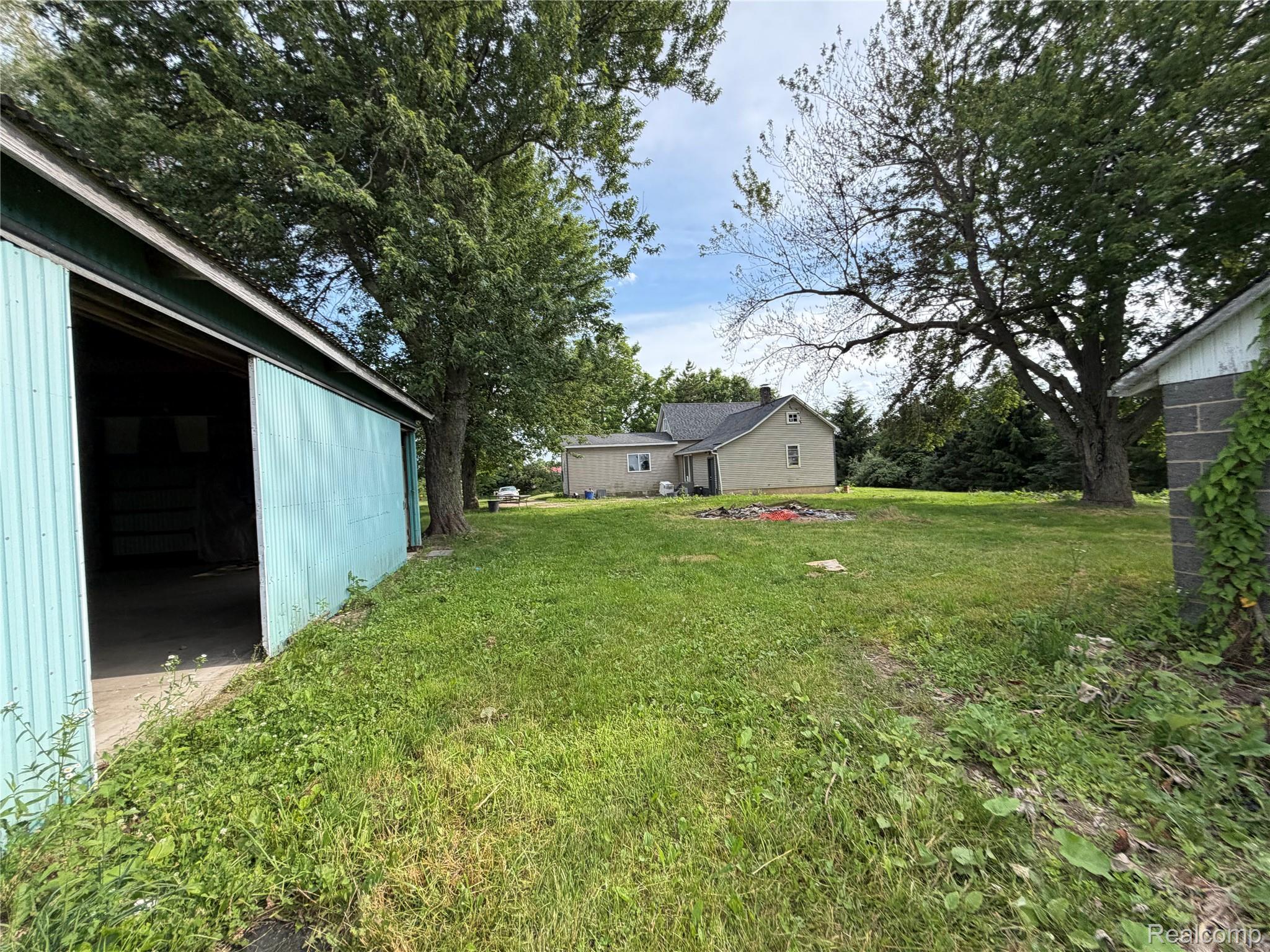 6447 Peck Road Marlette, MI 48453 - Photo 4 of 7 Spacious lot featuring a standalone residence, a large blue corrugated metal outbuilding with a sliding door, a block construction outbuilding, and mature trees