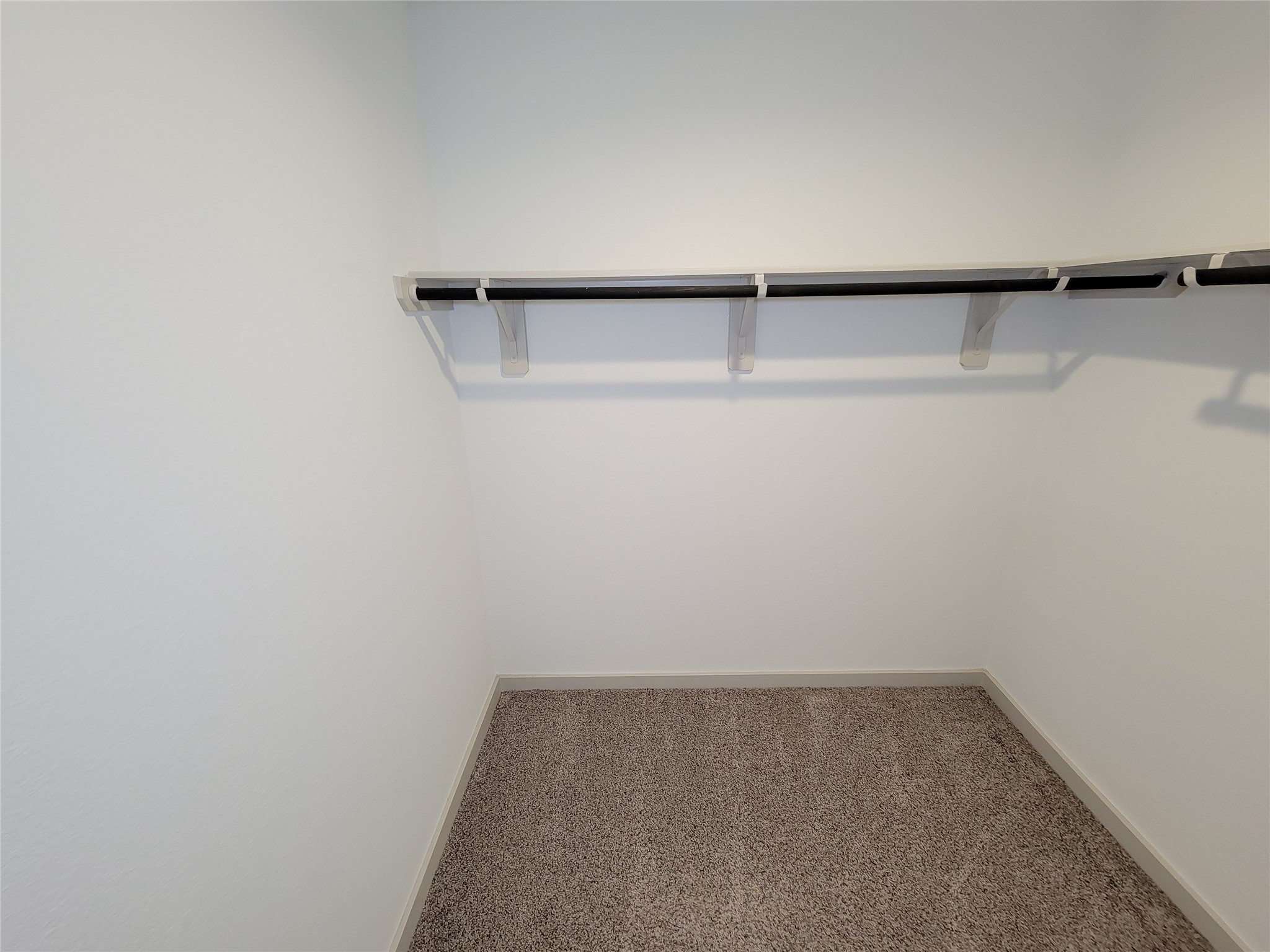 7722 Caldwell Crk Way Rosharon, TX 77583 - Photo 13 of 40 This photo shows a small, carpeted walk-in closet with a single hanging rod and shelf, ideal for organizing clothes and accessories.