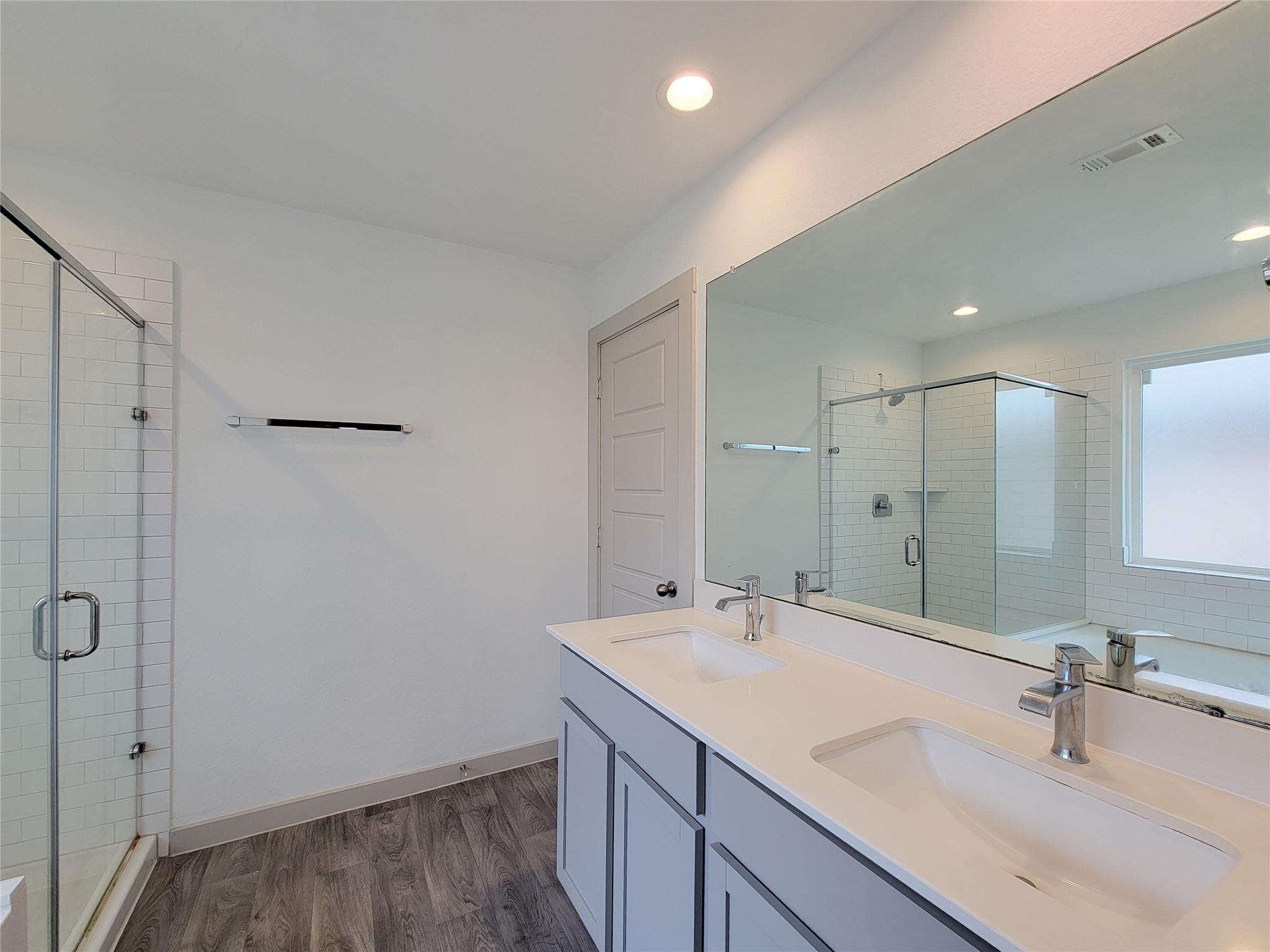 7722 Caldwell Crk Way Rosharon, TX 77583 - Photo 14 of 40 This bathroom features a sleek, modern design with a double vanity, large mirror, and a glass-enclosed walk-in shower. The space is bright and airy with wood-style flooring and neutral tones.