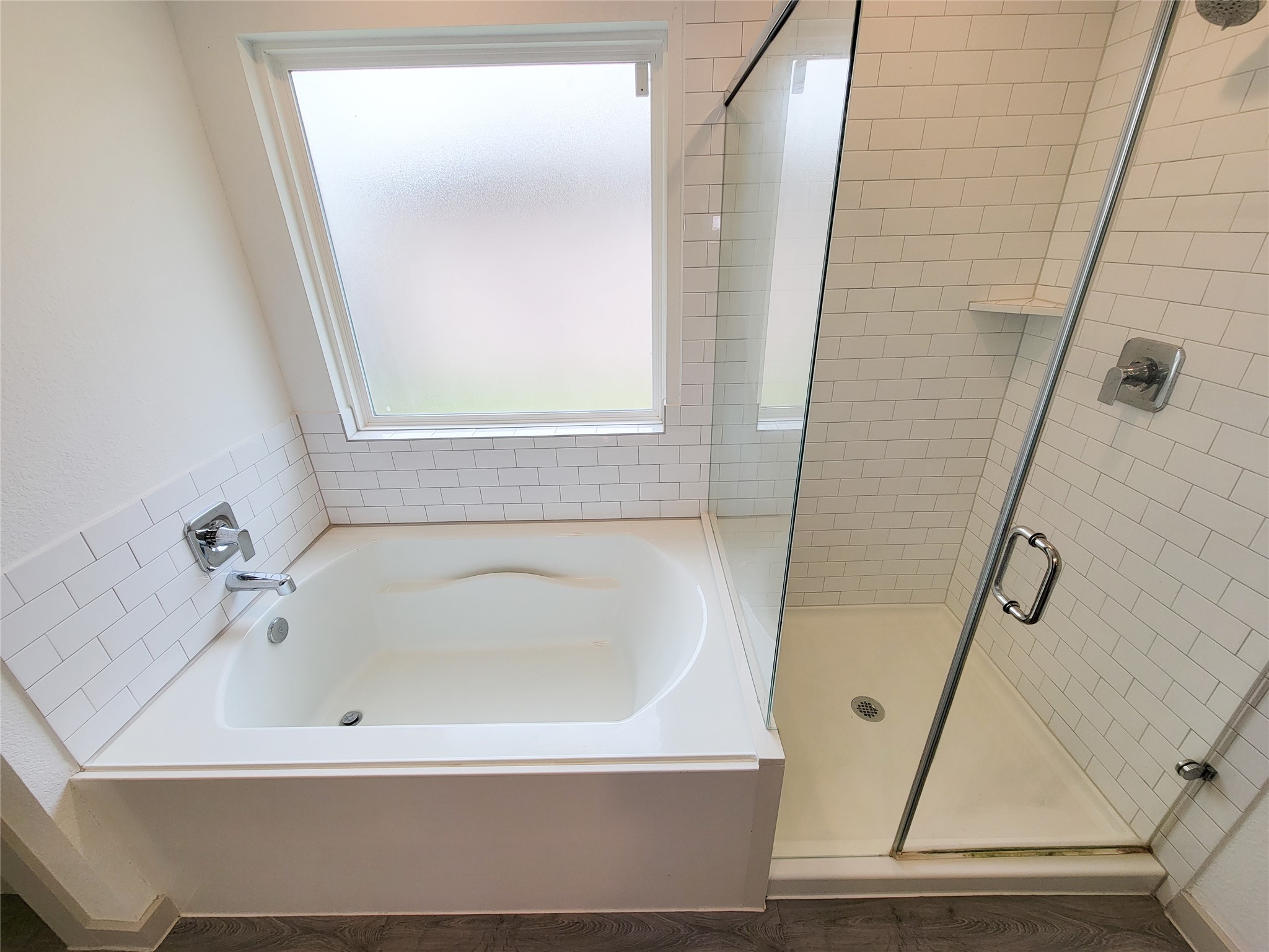 7722 Caldwell Crk Way Rosharon, TX 77583 - Photo 17 of 40 This bathroom features a clean, modern design with a spacious bathtub and a glass-enclosed shower. The white subway tiles and frosted window provide a bright and inviting atmosphere.