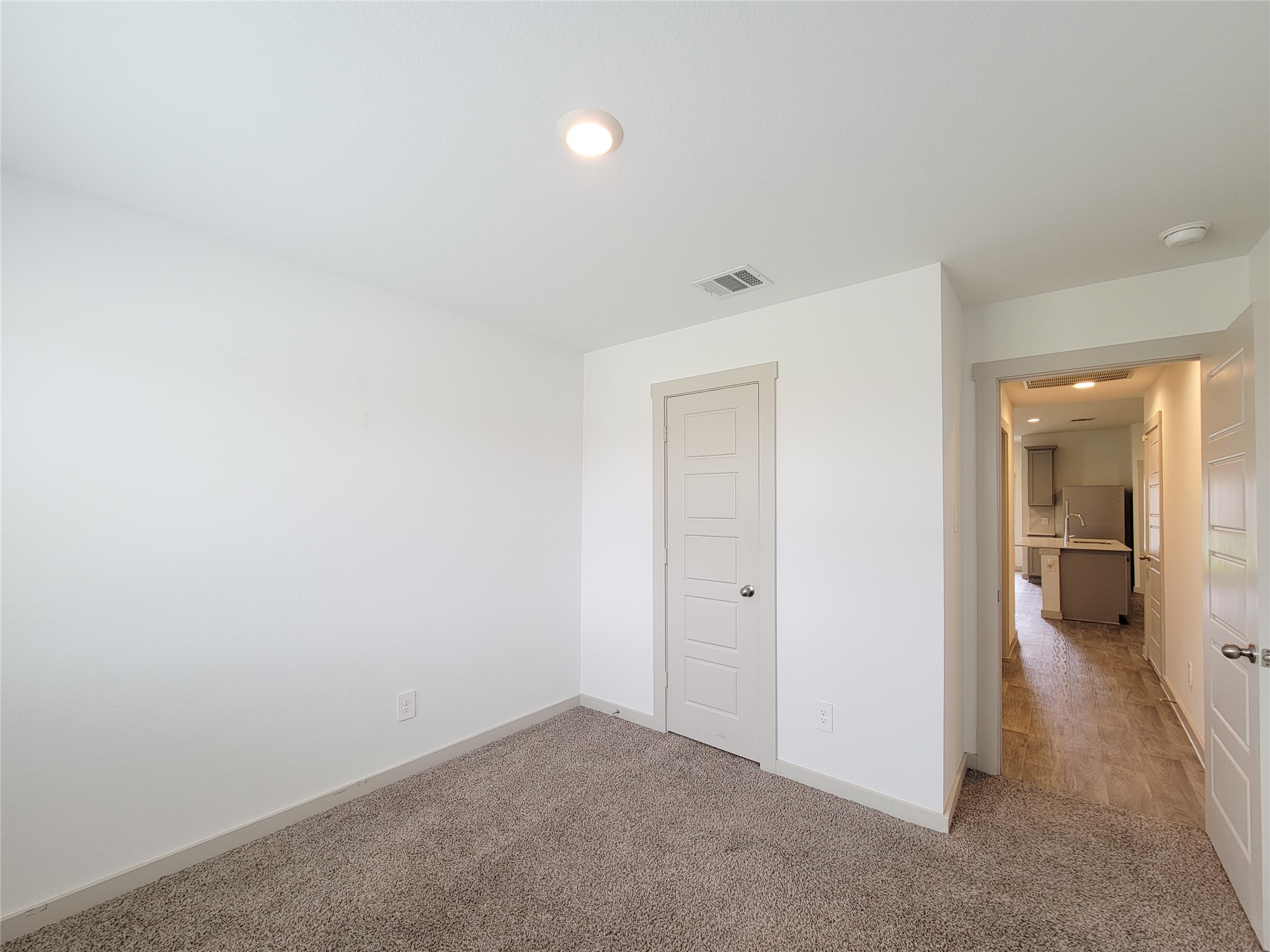 7722 Caldwell Crk Way Rosharon, TX 77583 - Photo 26 of 40 This photo shows a small, bright room with white walls and a carpeted floor. It features a ceiling light and a closet door, with a view into a hallway leading to the kitchen area.