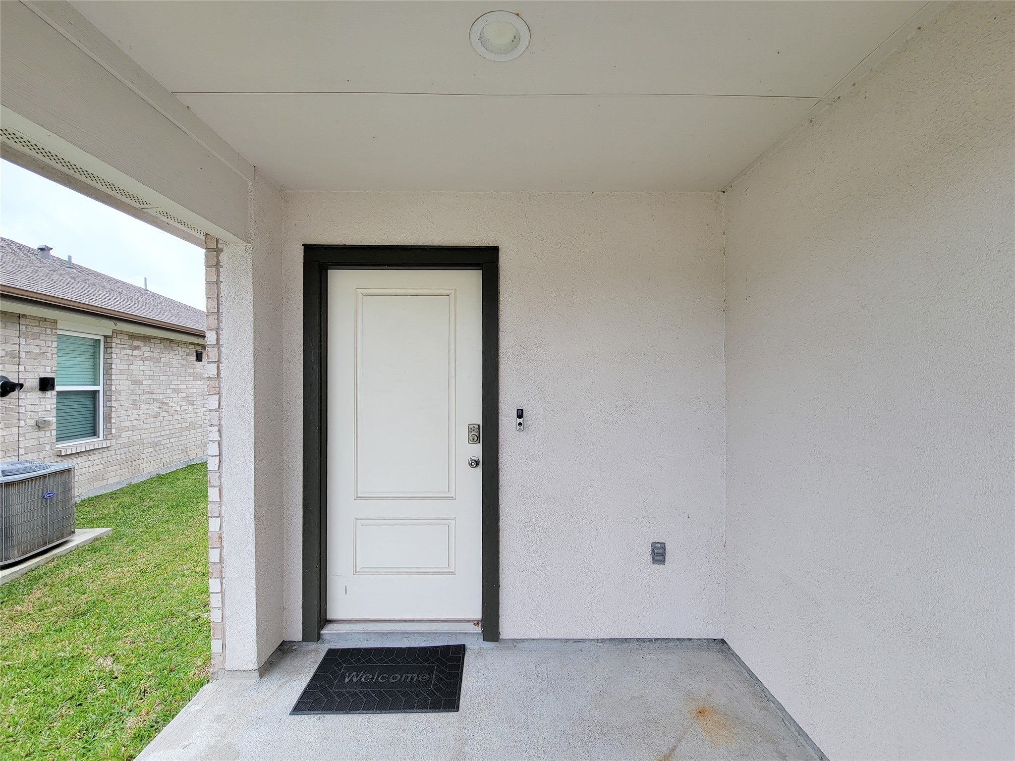 7722 Caldwell Crk Way Rosharon, TX 77583 - Photo 3 of 40 This photo shows a simple and covered entryway with a white door and a welcome mat. The exterior walls are light-colored, and there's a small patch of grass visible, suggesting a yard space.
