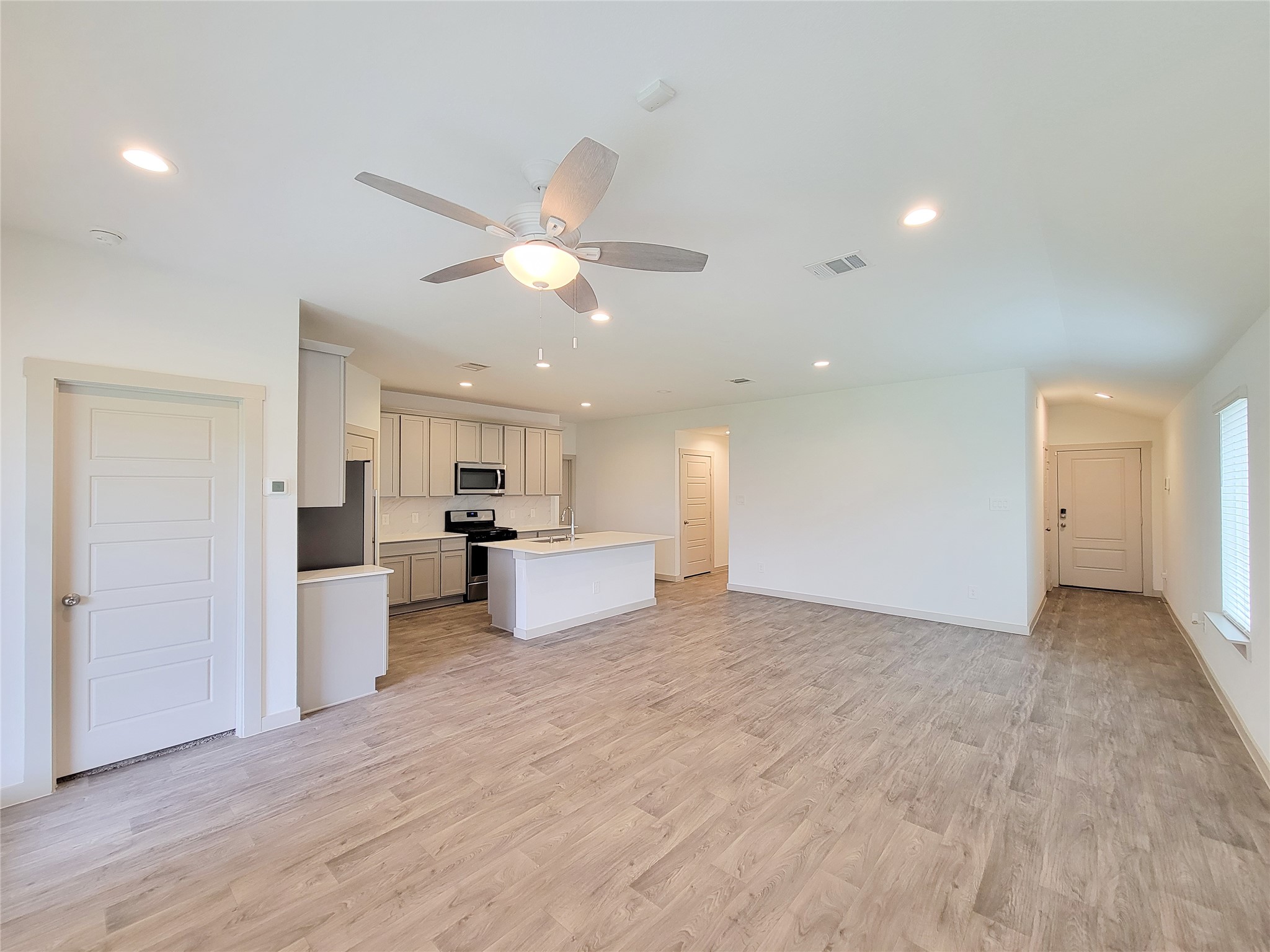 7722 Caldwell Crk Way Rosharon, TX 77583 - Photo 31 of 40 This spacious open-concept living area features modern wood-look flooring, recessed lighting, and a ceiling fan. The kitchen boasts sleek cabinetry, stainless steel appliances, and a central island, perfect for entertaining. The room is bright and inviting with large windows and neutral tones.