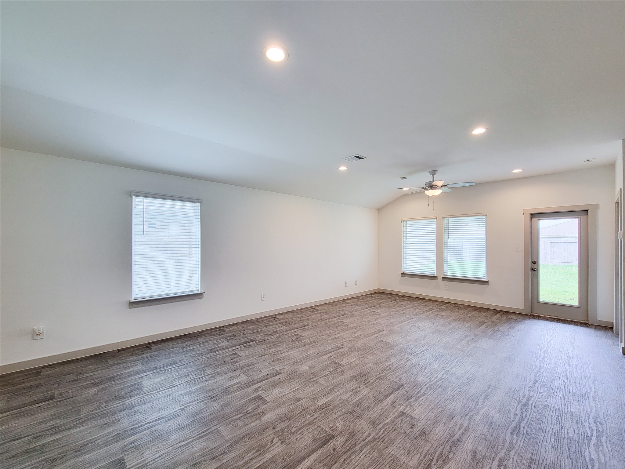 7722 Caldwell Crk Way Rosharon, TX 77583 - Photo 33 of 40 This spacious living area features modern wood flooring, recessed lighting, and ample natural light from large windows. A ceiling fan adds comfort, and a door leads to the outdoor space.