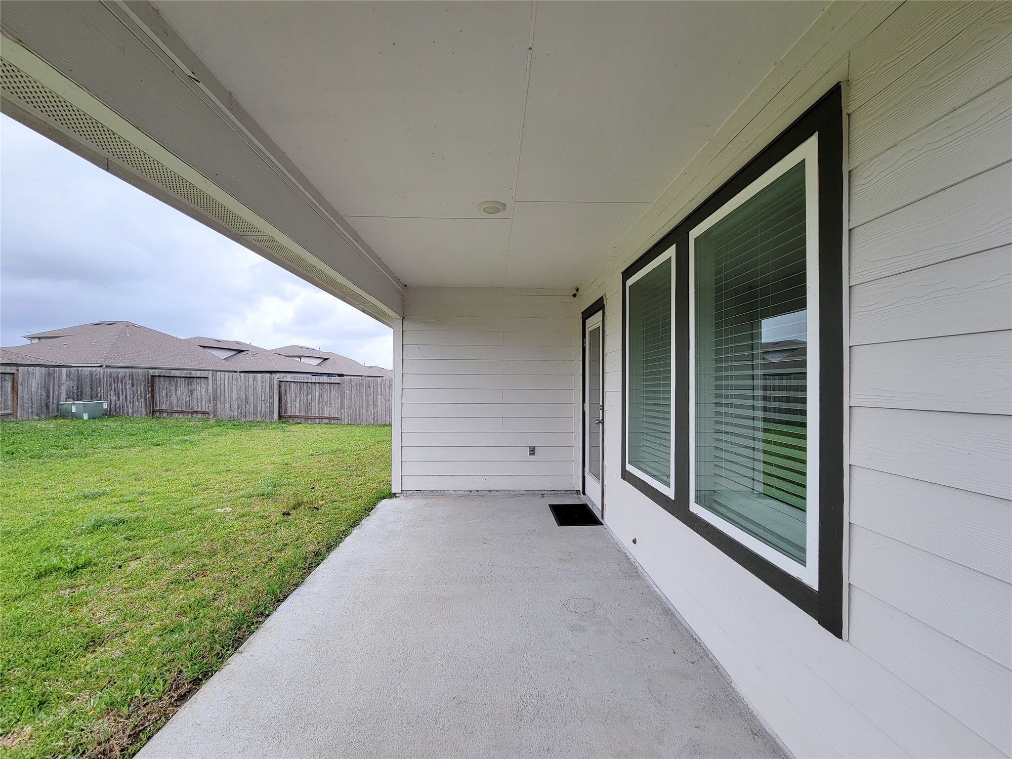 7722 Caldwell Crk Way Rosharon, TX 77583 - Photo 34 of 40 This photo shows a covered patio with a concrete floor, leading to a spacious backyard enclosed by a wooden fence. Large windows provide natural light to the interior, offering a great view of the outdoor space.