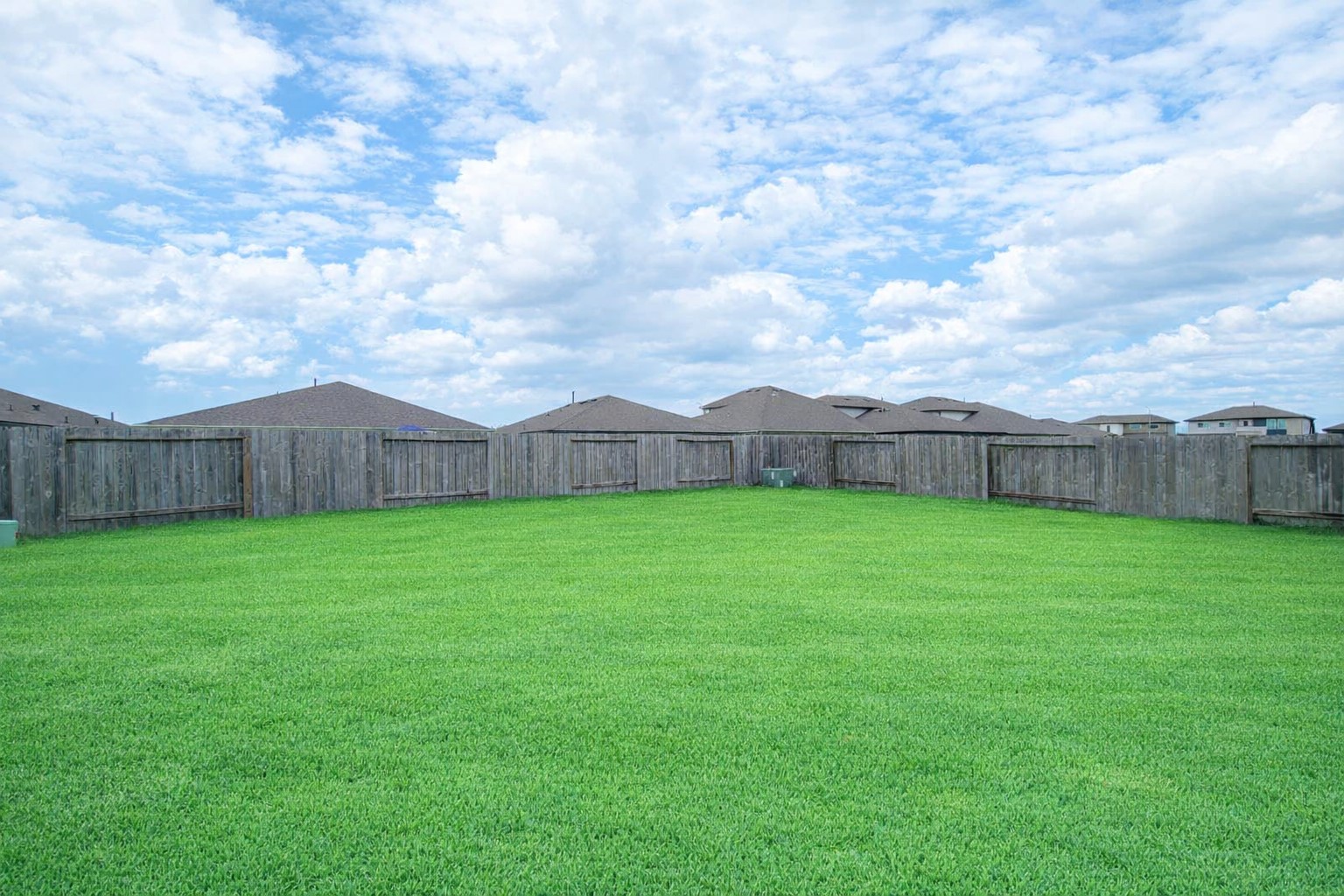 7722 Caldwell Crk Way Rosharon, TX 77583 - Photo 36 of 40 This photo showcases a spacious backyard with a well-maintained lawn, enclosed by a wooden fence, offering privacy and a serene view of a partly cloudy sky.