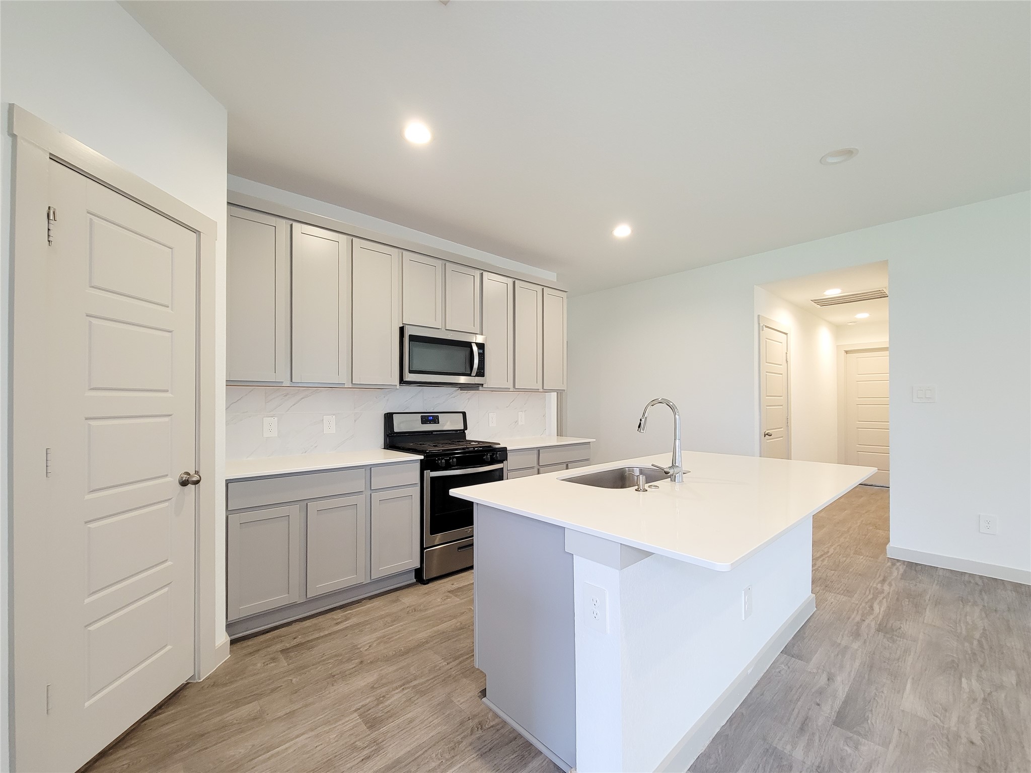 7722 Caldwell Crk Way Rosharon, TX 77583 - Photo 40 of 40 A modern kitchen with sleek gray cabinets, stainless steel appliances, and a large island with a sink. The space features light wood flooring and recessed lighting, creating a bright and inviting atmosphere.