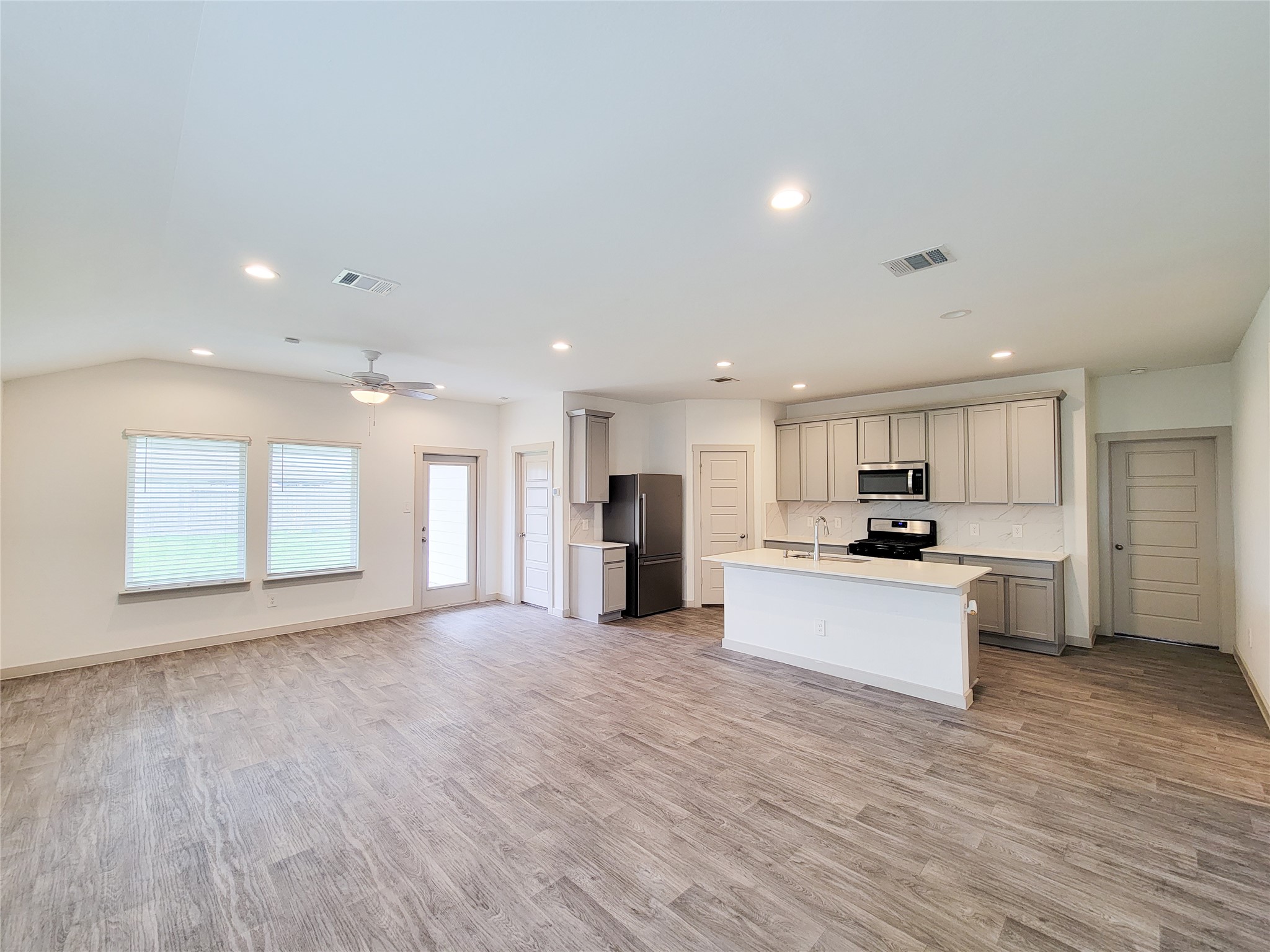 7722 Caldwell Crk Way Rosharon, TX 77583 - Photo 4 of 40 This photo showcases a modern, open-concept living area with a sleek kitchen. It features stainless steel appliances, ample cabinetry, recessed lighting, and wood-like flooring, creating a spacious and inviting atmosphere.