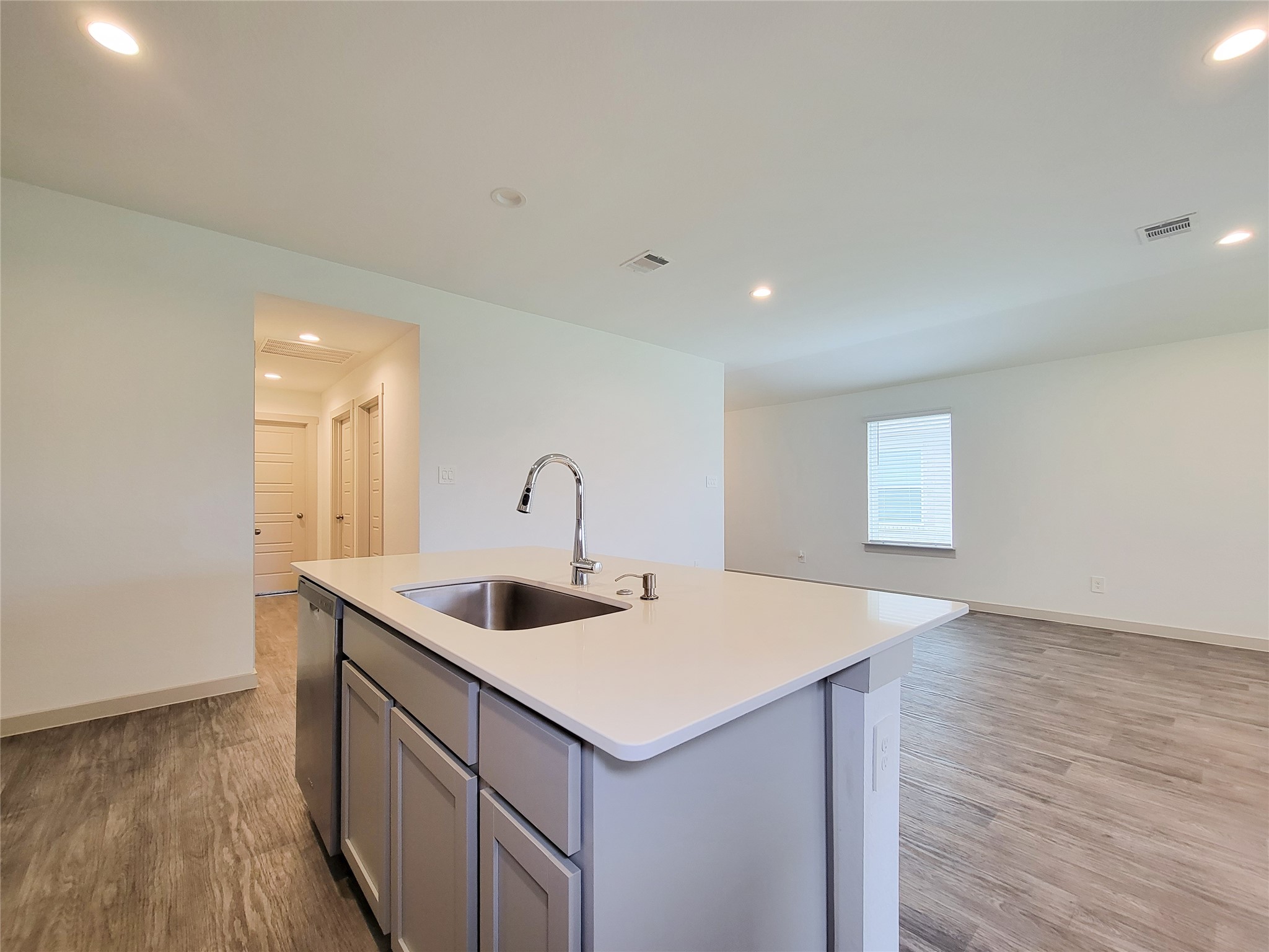 7722 Caldwell Crk Way Rosharon, TX 77583 - Photo 5 of 40 This photo showcases a modern open-plan kitchen and living area with sleek wood flooring. The kitchen features a central island with a sink and bright cabinetry. Ample natural light filters through a large window, creating an inviting atmosphere.