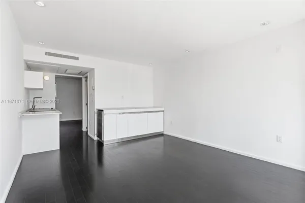 a view of empty room with wooden floor and kitchen