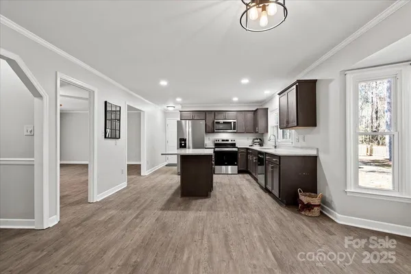 a kitchen with stainless steel appliances kitchen island granite countertop a stove a sink a refrigerator and white cabinets with wooden floor