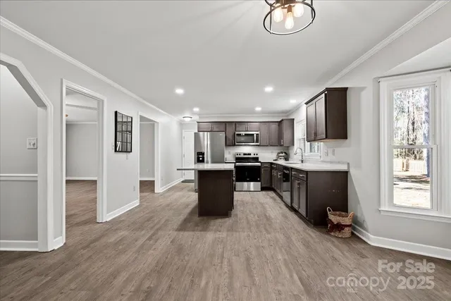 a kitchen with stainless steel appliances kitchen island granite countertop a stove a sink a refrigerator and white cabinets with wooden floor