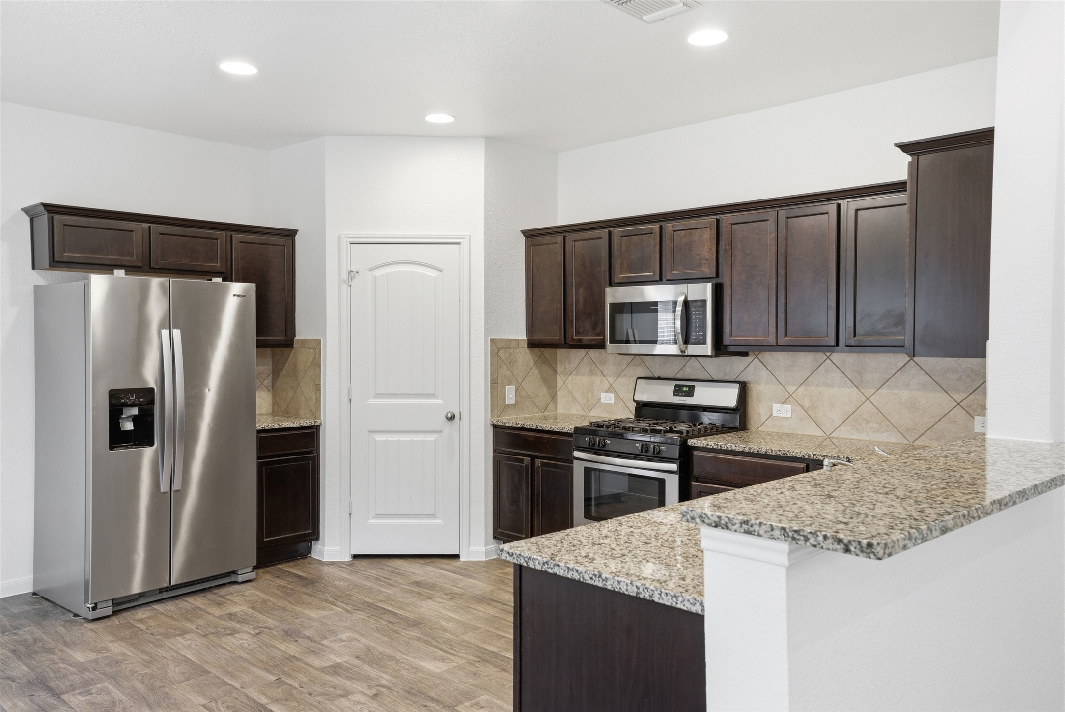 3009 Tilmon Ln. Austin, TX 78725 - Photo 4 of 33 Kitchen with stainless steel appliances, dark wood finish cabinetry, a peninsula, light stone countertops, and light wood-style floors