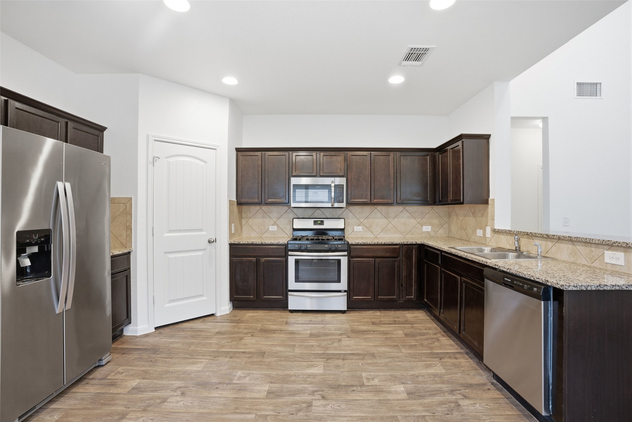3009 Tilmon Ln. Austin, TX 78725 - Photo 5 of 33 Kitchen featuring stainless steel appliances, dark wood finish cabinetry, light wood-style flooring, light stone counters, and decorative backsplash