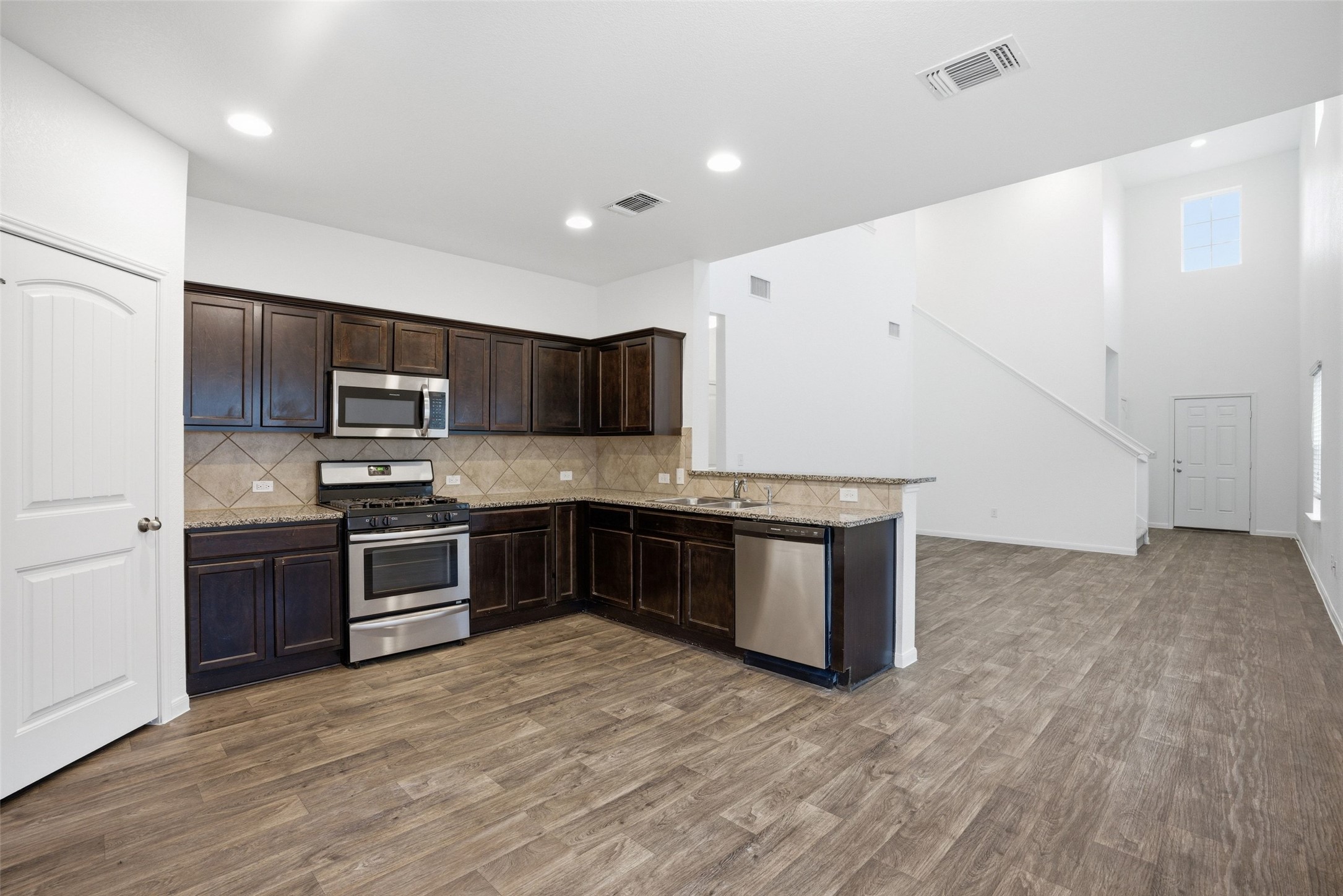 3009 Tilmon Ln. Austin, TX 78725 - Photo 6 of 33 Kitchen featuring stainless steel appliances, dark wood finish cabinets, light stone counters, a peninsula, and backsplash