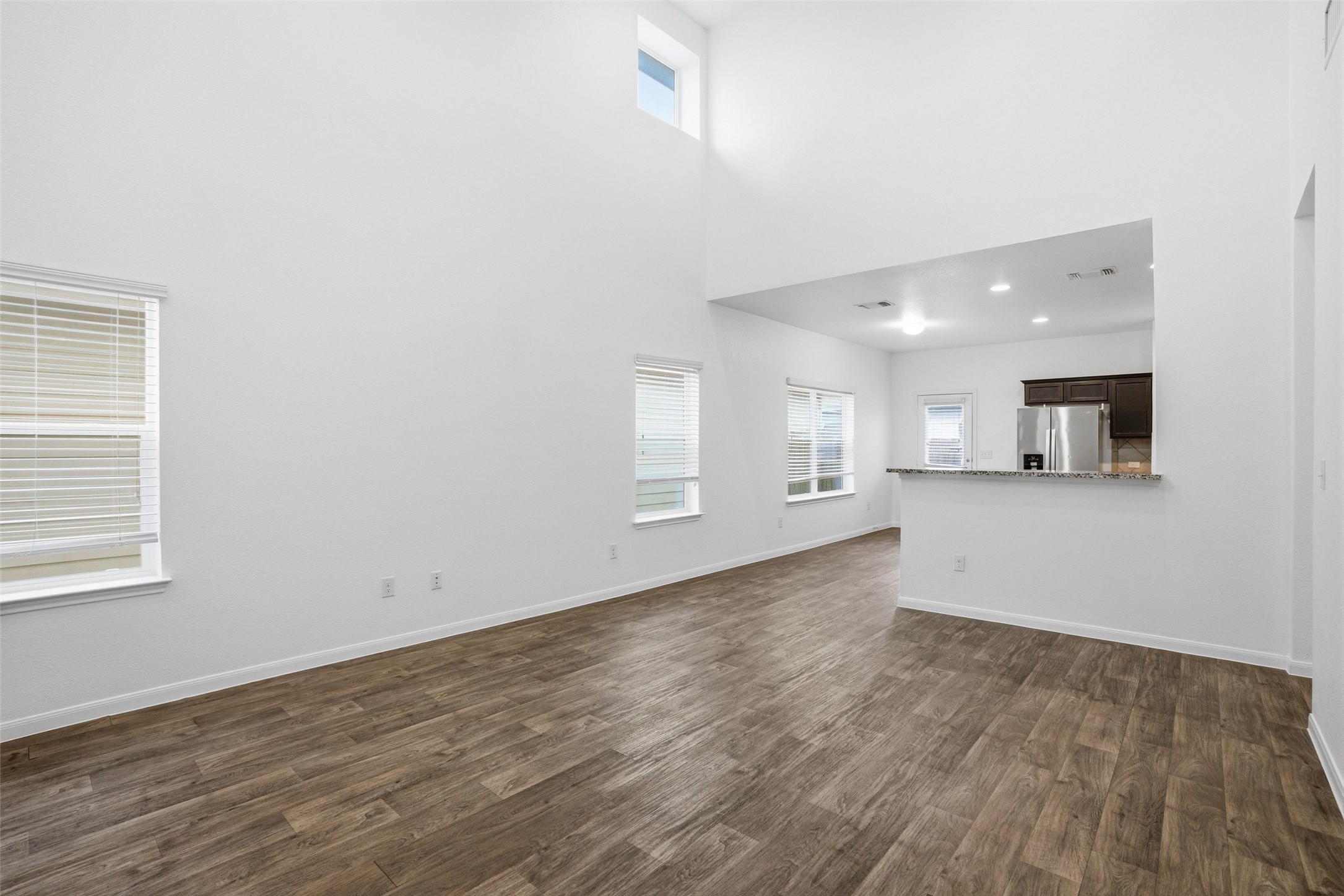 3009 Tilmon Ln. Austin, TX 78725 - Photo 9 of 33 Unfurnished living room featuring healthy amount of natural light, dark wood-type flooring, a high ceiling, and recessed lighting