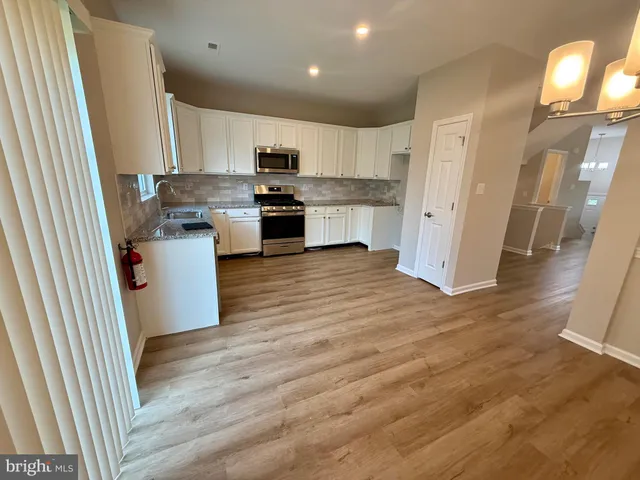 a kitchen with granite countertop white cabinets a sink dishwasher and a stove with wooden floor