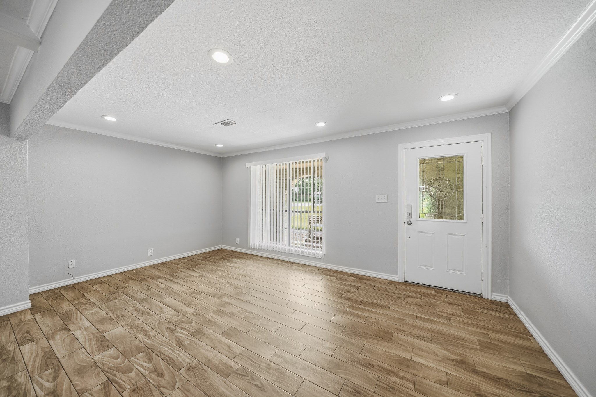 302 Country Road 893 Angleton, TX 77515 - Photo 9 of 26 Bright and spacious living area with wood-like flooring, recessed lighting, and a window with vertical blinds. The space features a white front door with decorative glass, offering a welcoming entrance.