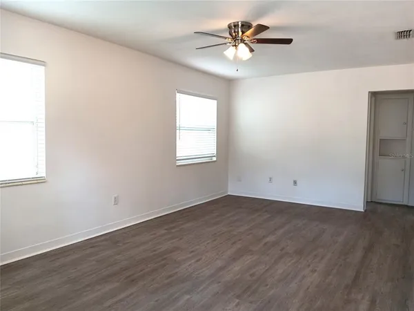 an empty room with wooden floor chandelier fan and windows