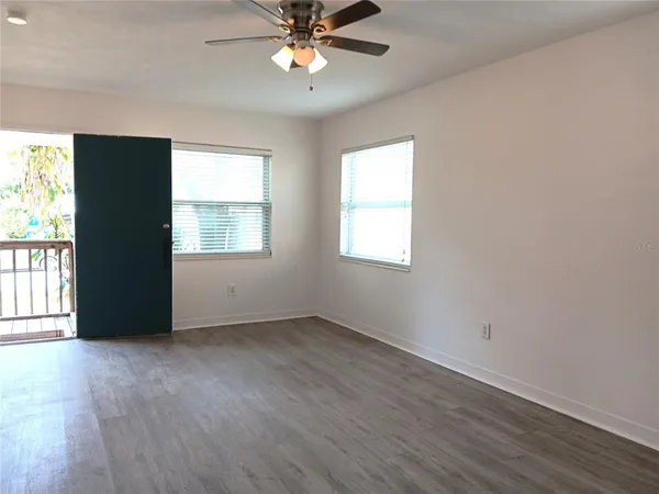 an empty room with wooden floor fan and windows