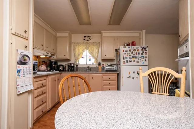 a kitchen with stainless steel appliances kitchen island granite countertop a refrigerator a stove a sink and white cabinets with wooden floor